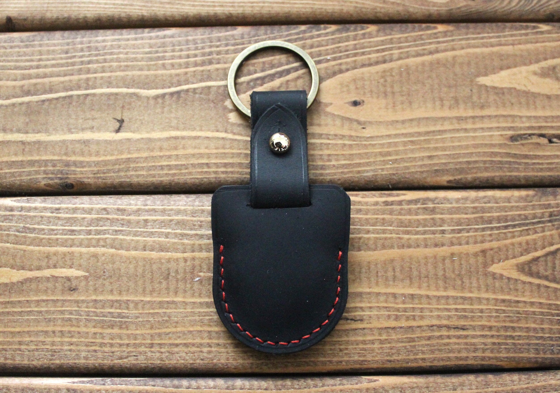 A black full-grain leather case for an AirTag with a metal keyring, The case has red stitching detail