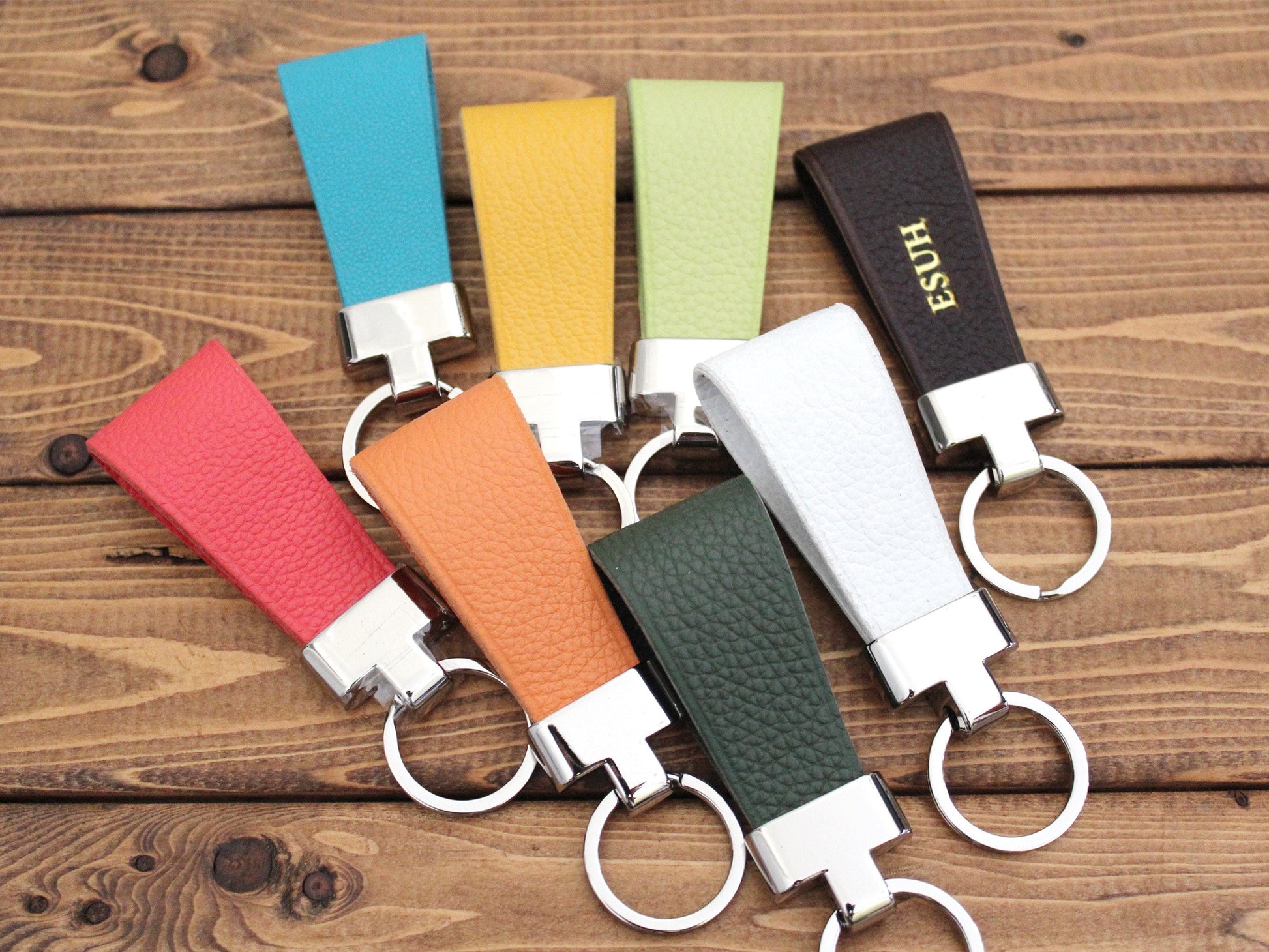A variety of colorful leather keychains with metal rings, displayed on a wooden surface.