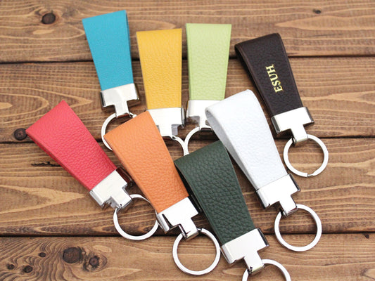 A variety of colorful leather keychains with metal rings, displayed on a wooden surface.