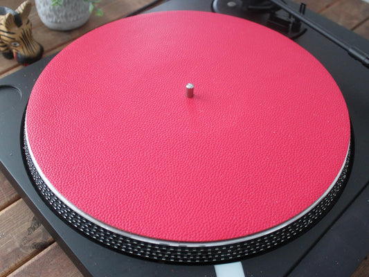 A pink red leather turntable platter mat placed on a record player.